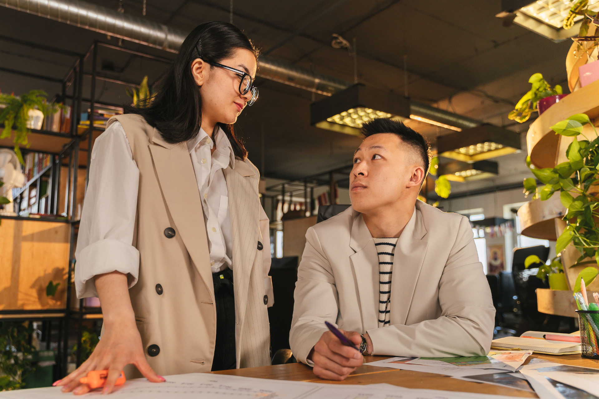 Two professionals reviewing plans and documents together at a desk in a warm, plant-filled office
